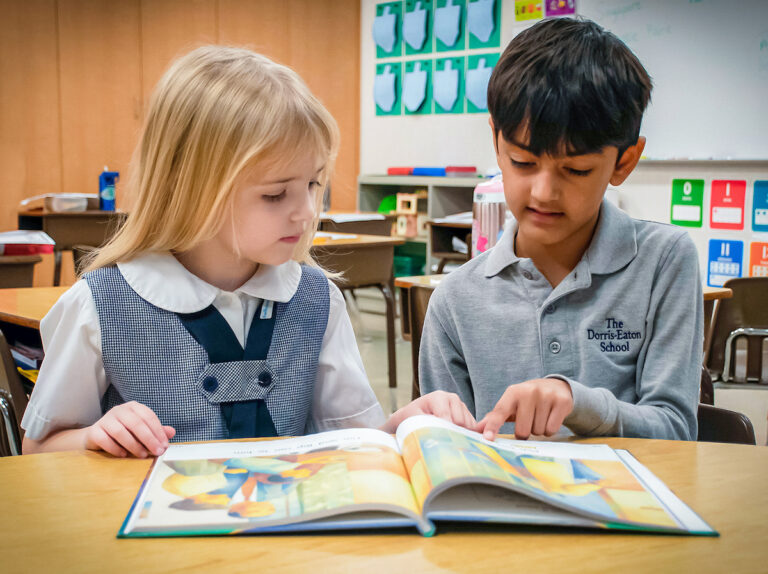 Two kindergartners sittig side by side, reading a colorful storybook.